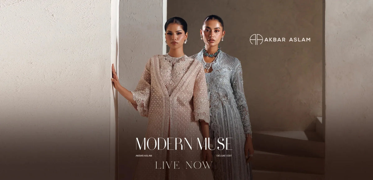 Two models wearing traditional Indian salwar kameez outfits by Akbar Aslam Modern Muse. The model in the foreground wears a sage green embroidered jacket with a matching pleated skirt, while the model in the background wears a dusty rose embroidered jacket with a matching skirt.1621243260e1af0c20-2